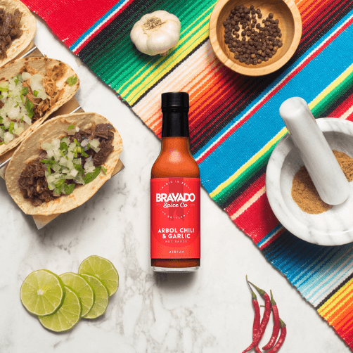 Bravado Spice Co’s Árbol Chili & Garlic Hot Sauce alongside different varieties of tacos.