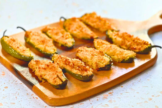 Golden-brown jalapeño poppers on a wooden board, topped with panko breadcrumbs.