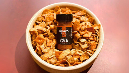 Cheesy taco–style spicy snack mix in a bowl with Bravado Spice Co.’s Garlic & Arbol Seasoning placed in the center.