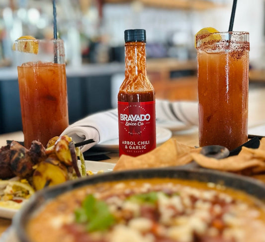 Bravado Spice Co.’s Árbol Chilli & Garlic Hot Sauce surrounded by two Bloody Marys.