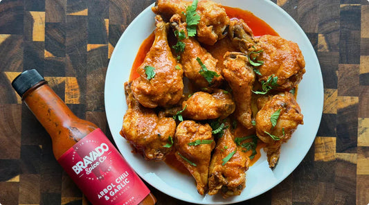 A plate of crispy oven-baked Arbol Chili & Garlic wings beside Bravado Spice Co.’s hot sauce bottle.
