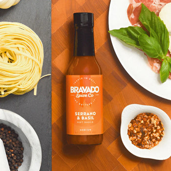 Bravado Spice Serrano & Basil Hot Sauce alongside fresh basil, cured meat, pasta, and spices for Italian cooking.