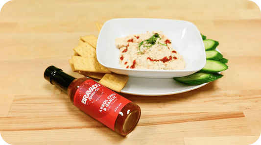 smoked salmon dip in a bowl with crackers and cucumbers, bottle of Arbol Chili & Garlic Hot Sauce