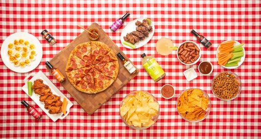 Overhead view of a table spread with pepperoni pizza, wings, snacks, and various Bravado Spice hot sauces.