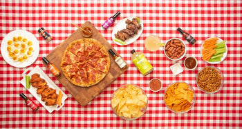 Overhead view of a table spread with pepperoni pizza, wings, snacks, and various Bravado Spice hot sauces.