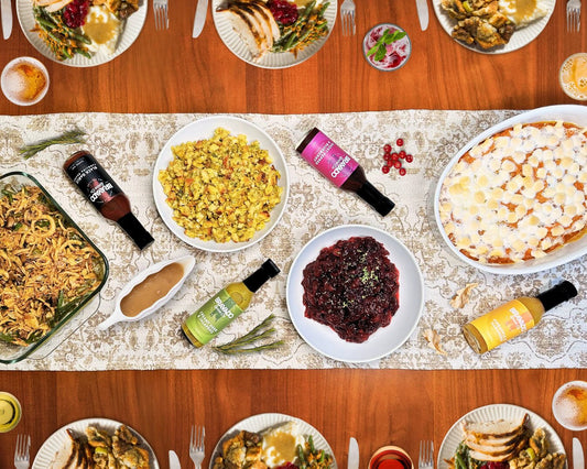 An overhead Thanksgiving feast with turkey, sides, and four bottles of Bravado Spice Co. hot sauces on a table runner.