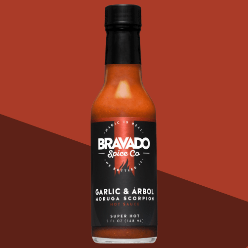 A bottle of Bravado Spice Co. Garlic & Árbol Moruga Scorpion Hot Sauce, featuring smoky garlic and chili flavor with bold red packaging.